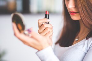 woman holding lipstick and looking at mirror